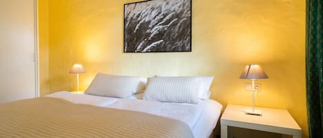 Habitación de hotel con cama, dos lámparas de noche, una mesita de noche y un cuadro en la pared.