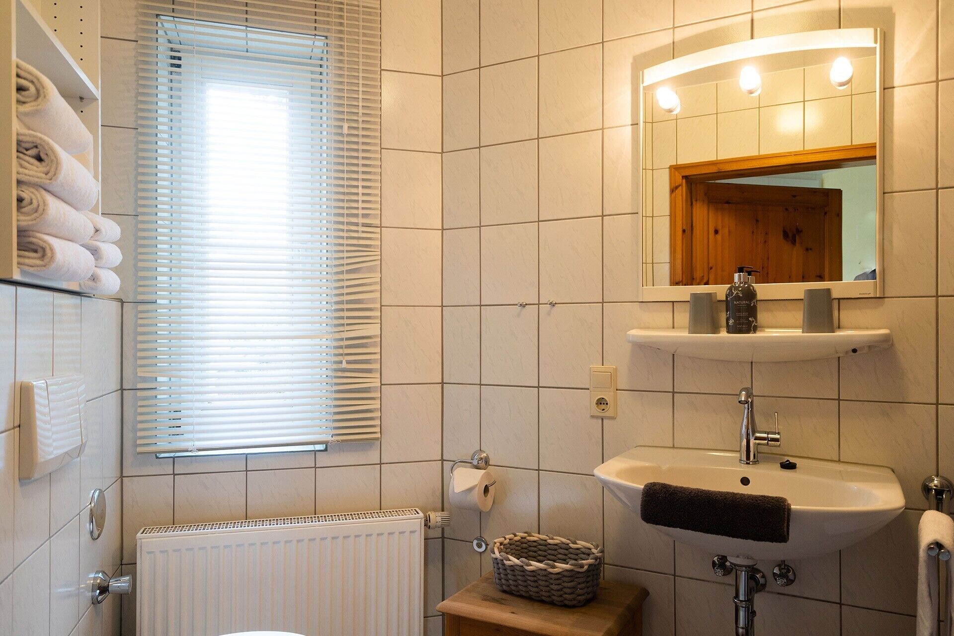 Ein Badezimmer mit Toilette, Waschbecken, Spiegel, Handtuchhalter und einem Fenster mit Jalousien.