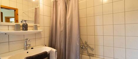 A bathroom with a sink, mirror, and shower.