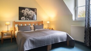 Un dormitorio con una cama, dos mesitas de noche, una lámpara de noche, una ventana con cortinas y un cuadro colgado en la pared.