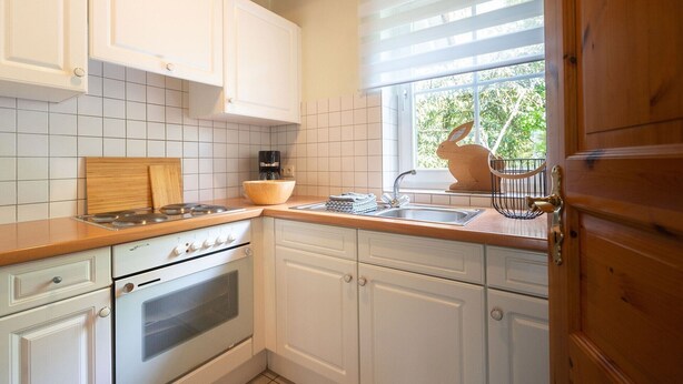 Una cocina con armarios blancos, una encimera de madera, estufa, horno, fregadero y una ventana con persianas.