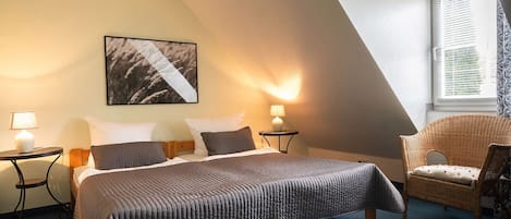 A bedroom with a bed, two bedside tables with lamps, a chair, a window with blinds, and a wall-mounted picture.