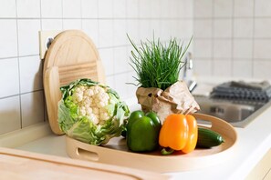 Eine Küchenarbeitsplatte mit Schneidebrett, einem Blumenkohl, einem Bund grüner Kräuter und ein paar Paprika.