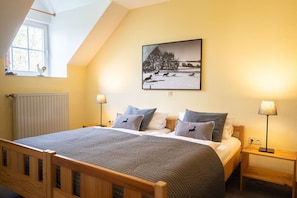 Ein Schlafzimmer mit einem Bett, zwei Nachttischen, einem Fenster, einer Heizung und einem Wandbild.