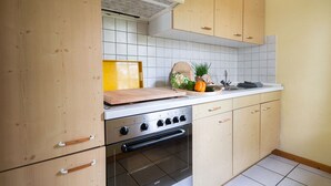 Ett kök med träskåp, en spis i rostfritt stål och en kakelbeklädd vägg bakom arbetsbänken.