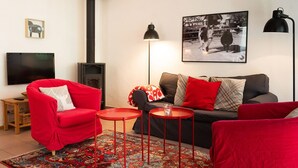 Ein Wohnzimmer mit einem roten Sofa, einem grauen Sofa, einem roten Couchtisch, einer schwarzen Lampe, einem gerahmten Bild und einem Kamin.