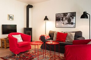 Una sala de estar con un sofá rojo, un sofá gris, una mesita de centro roja, una lámpara negra, un cuadro enmarcado y una chimenea.