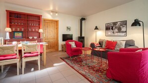 Ein Wohnzimmer mit einem roten Sofa, einem Holzespeisetisch mit Stühlen, einem roten Teppich und einem Bücherregal mit Gläsern.