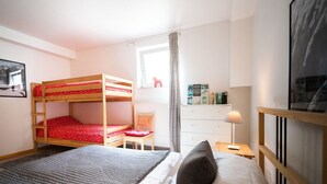Ein Schlafzimmer mit Etagenbetten, einem Schreibtisch, einem Stuhl, einer Kommode und einer Lampe.