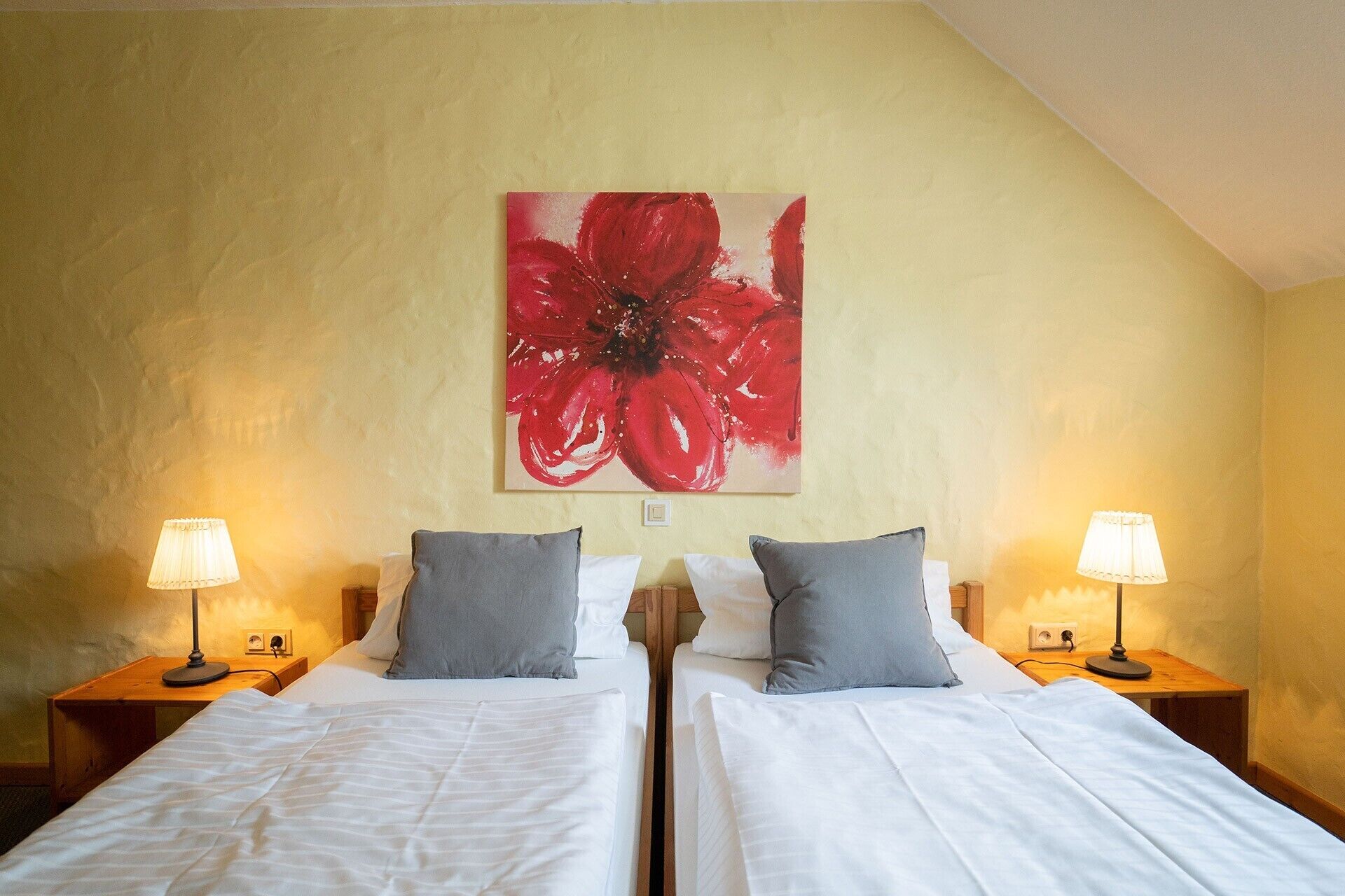 Una camera d'albergo con due letti, un'ampia opera d'arte floreale rossa sulla parete e due lampade da comodino.