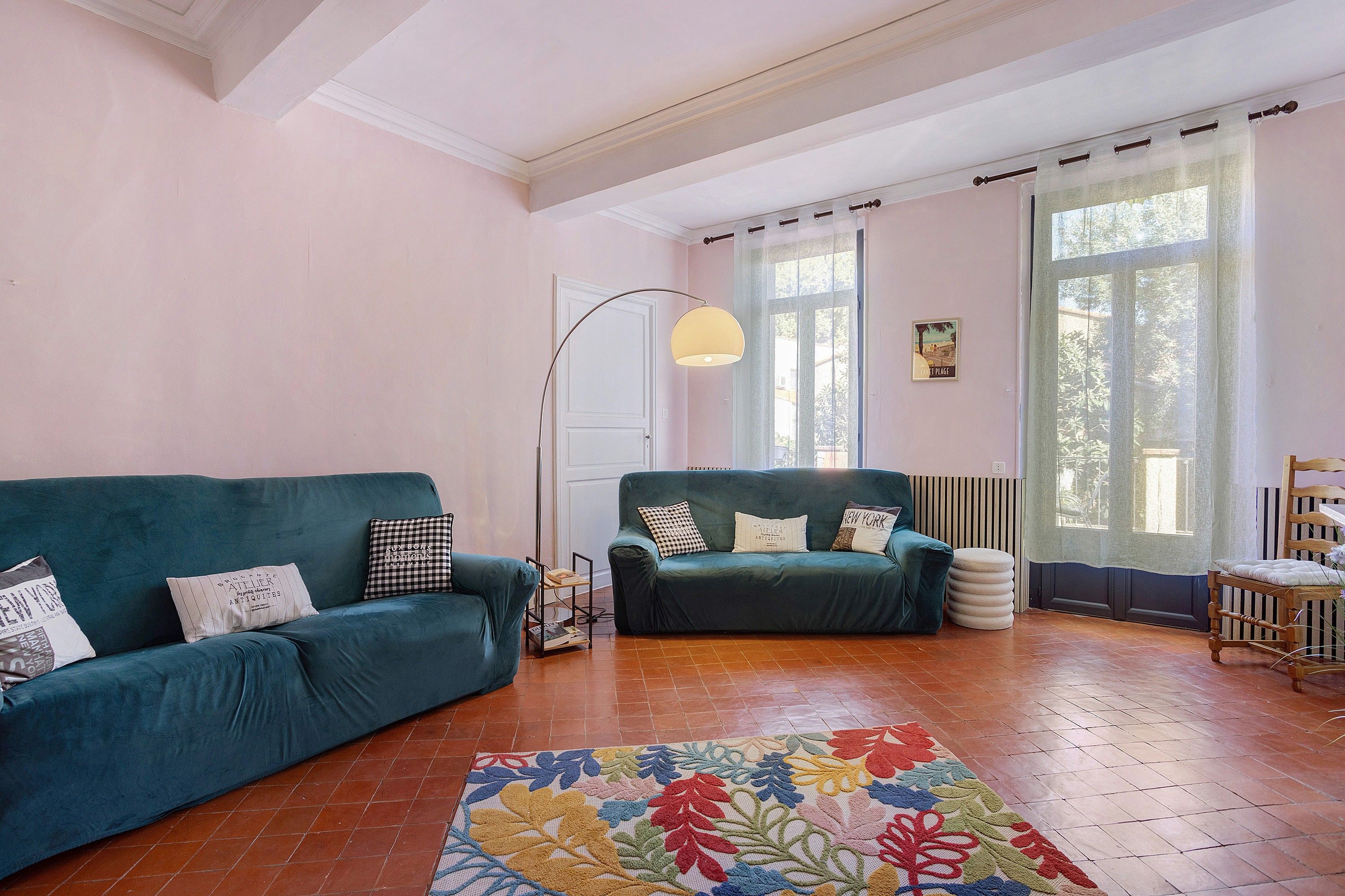 Un amplio salón con dos sofás, una lámpara de pie y un ventanal con cortinas.