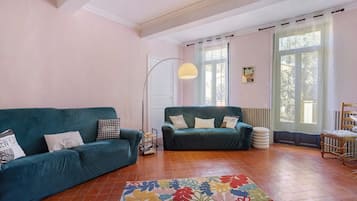 Un amplio salón con dos sofás, una lámpara de pie y un ventanal con cortinas.
