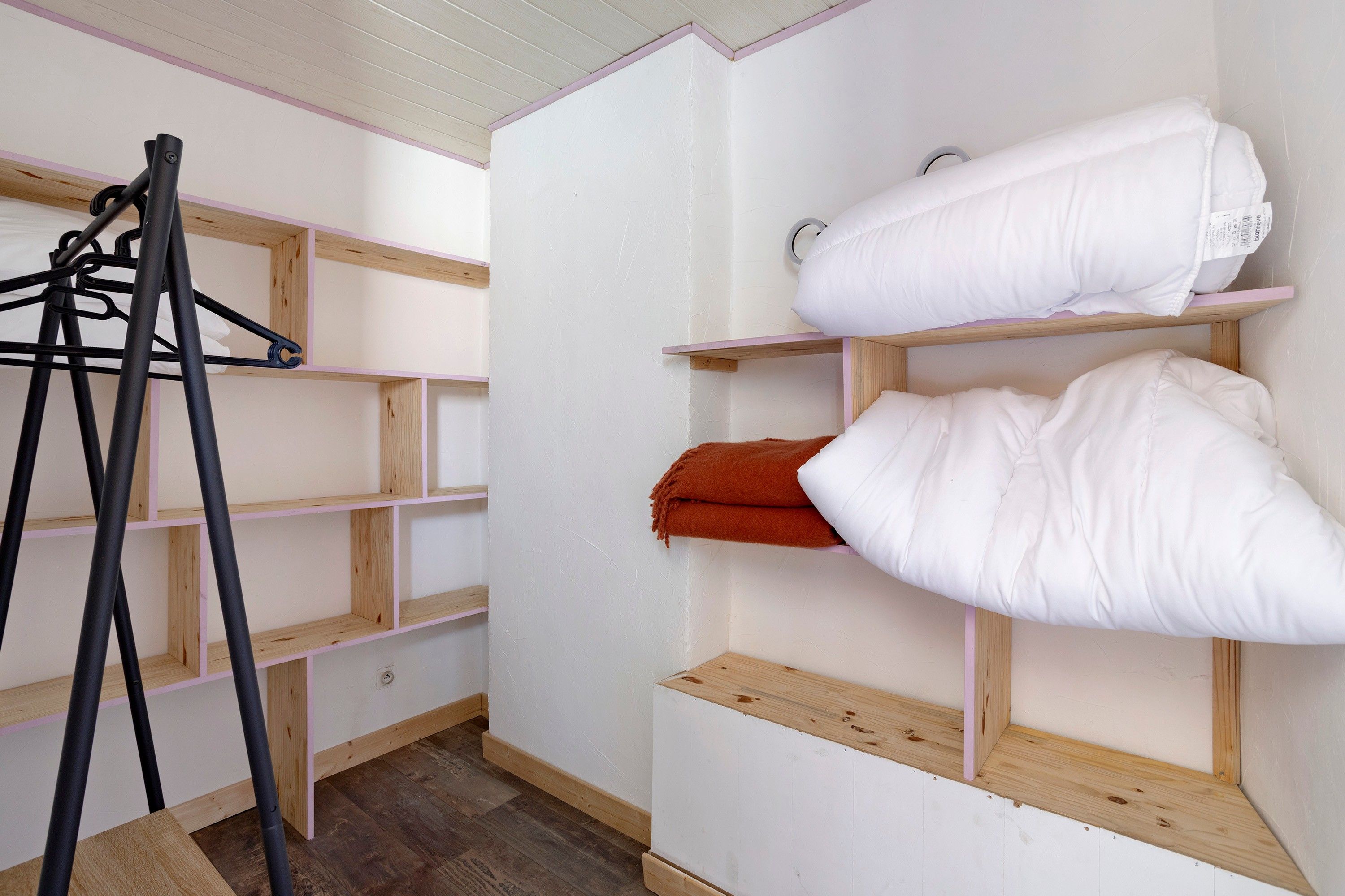 A room with wooden shelving units, a coat rack, and a bed with white bedding.