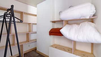 A room with wooden shelving units, a coat rack, and a bed with white bedding.