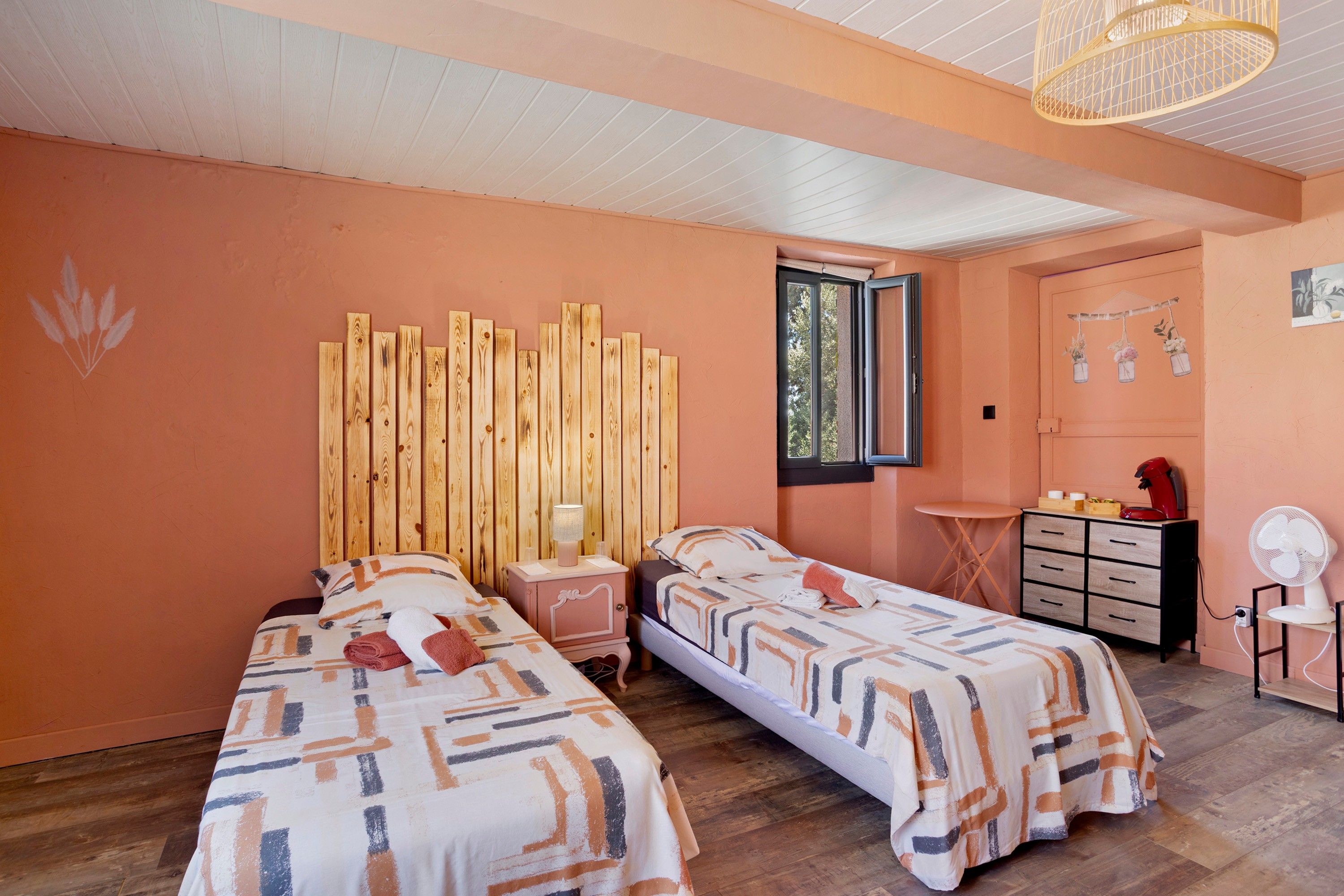 A room with two beds, a wooden headboard, a small table, a chair, and a window.