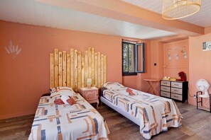 A room with two beds, a wooden headboard, a small table, a chair, and a window.