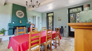 Un comedor con mantel rojo, sillas de madera, una araña y un reloj en la pared.