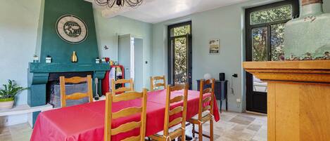 A dining room with a red tablecloth, wooden chairs, a chandelier, and a clock on the wall.