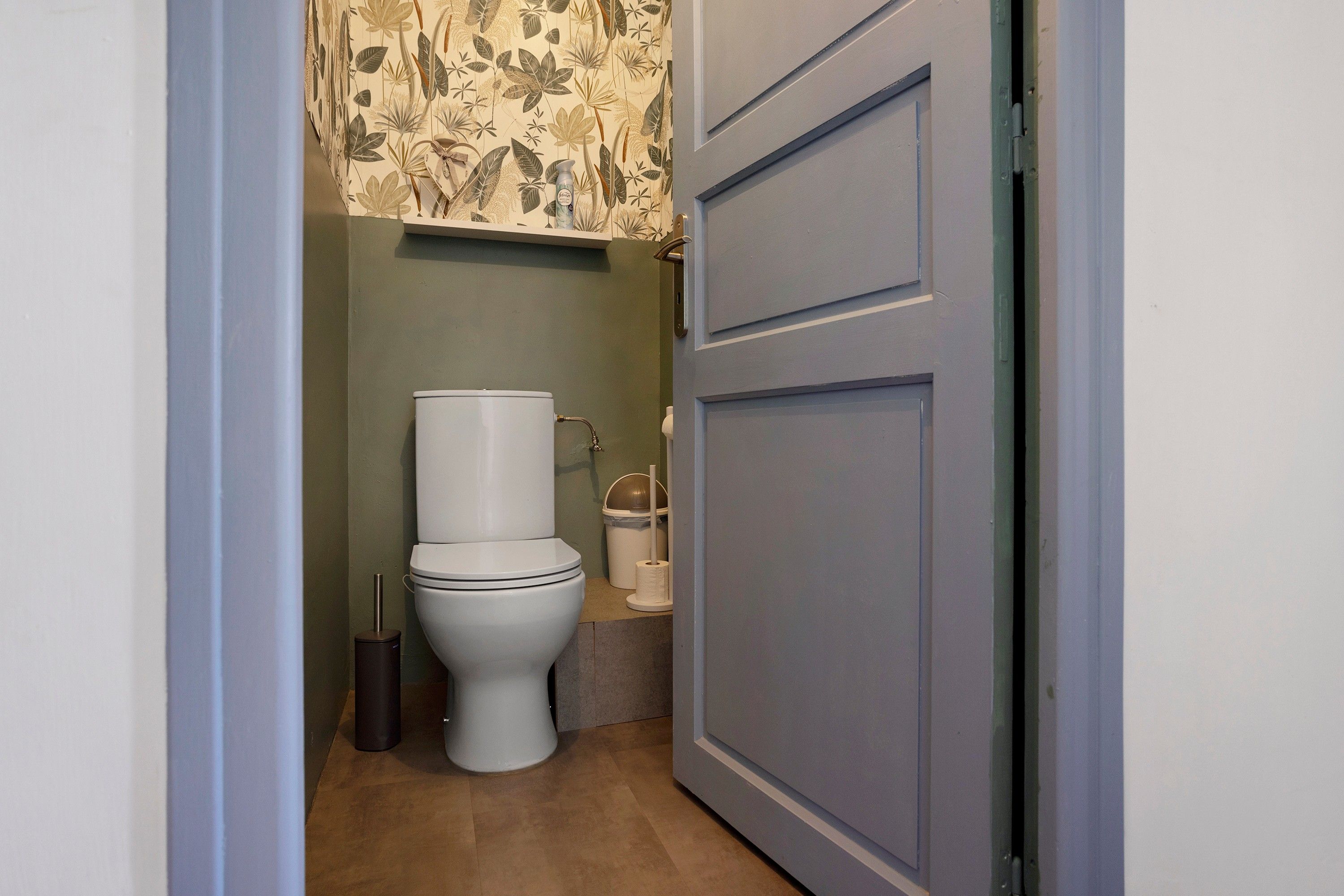 Een kleine badkamer met een toilet, een prullenbak en een toiletrolhouder.