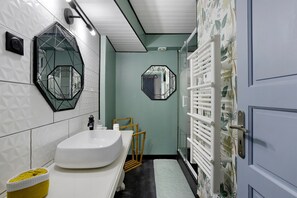 Un baño con un lavamanos blanco, un espejo y una zona de ducha con un toallero blanco.