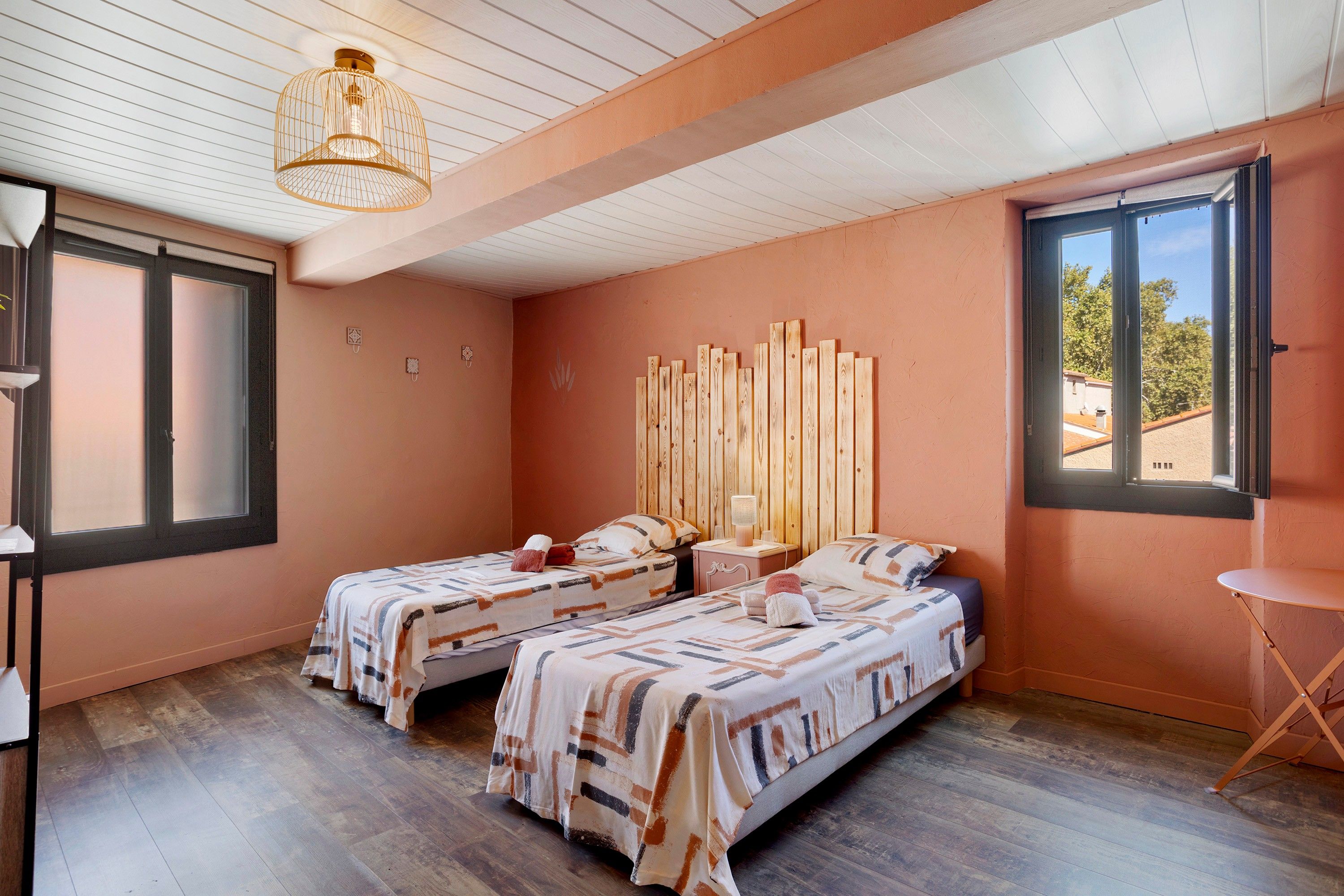 Una habitación con dos camas, un cabecero de madera, una mesita pequeña y una ventana.