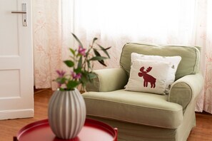 Ein Zimmer mit einem grünen Sofa, einem weißen Kissen mit Elch-Motiv, einer gestreiften Vase mit Blumen und einem roten Tablett.