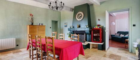 A dining area with a table set for four, wooden chairs, a chandelier, a clock on the wall, and a red tablecloth.