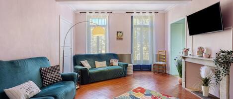 A living room with a green sofa, a small table, a floor lamp, and a television on the wall.