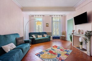 Una sala de estar con un sofá verde, una mesita, una lámpara de pie y un televisor en la pared.
