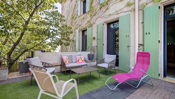 Un espacio al aire libre con sofá y sillones, una mesita pequeña y una butaca rosa.