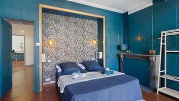 Un dormitorio con papel tapiz estampado, una cama con ropa de cama azul, un radiador blanco y un estante blanco.