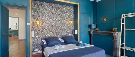 A bedroom with a patterned wallpaper, a bed with blue bedding, a white radiator, and a white shelf unit.