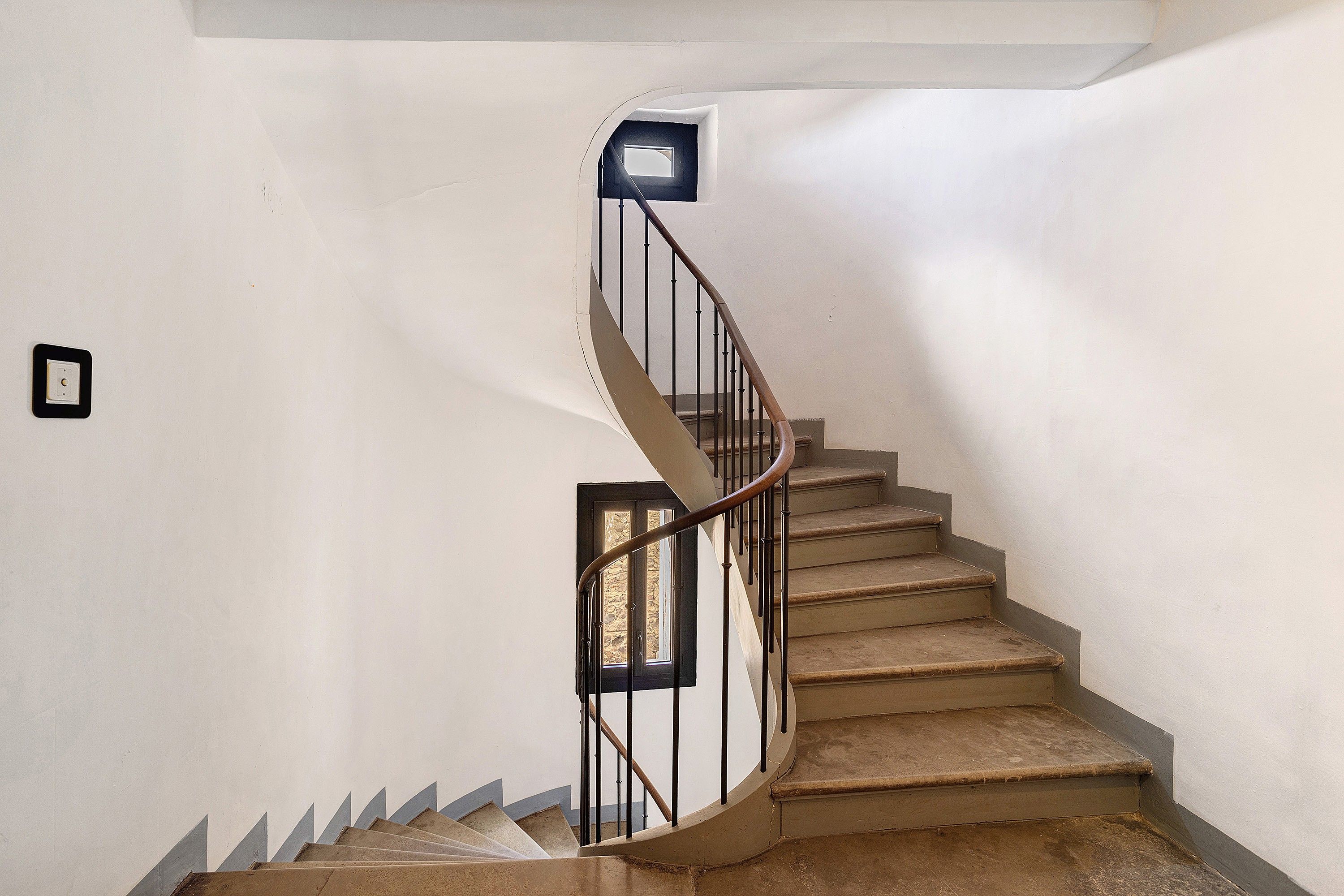 Una escalera de caracol con barandilla y una lámpara en la pared.
