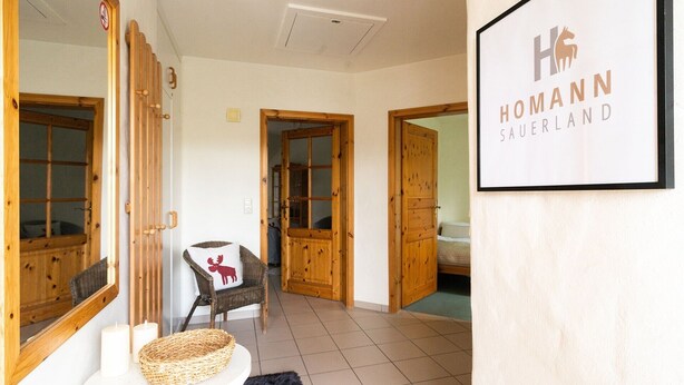 A hotel interior with wooden doors, a framed sign, a wicker basket, and a chair with a red pillow. - Apartment 'Ferienhof Homann Sauerland - LH 6 Balcony and Wi-Fi' (Brilon)
