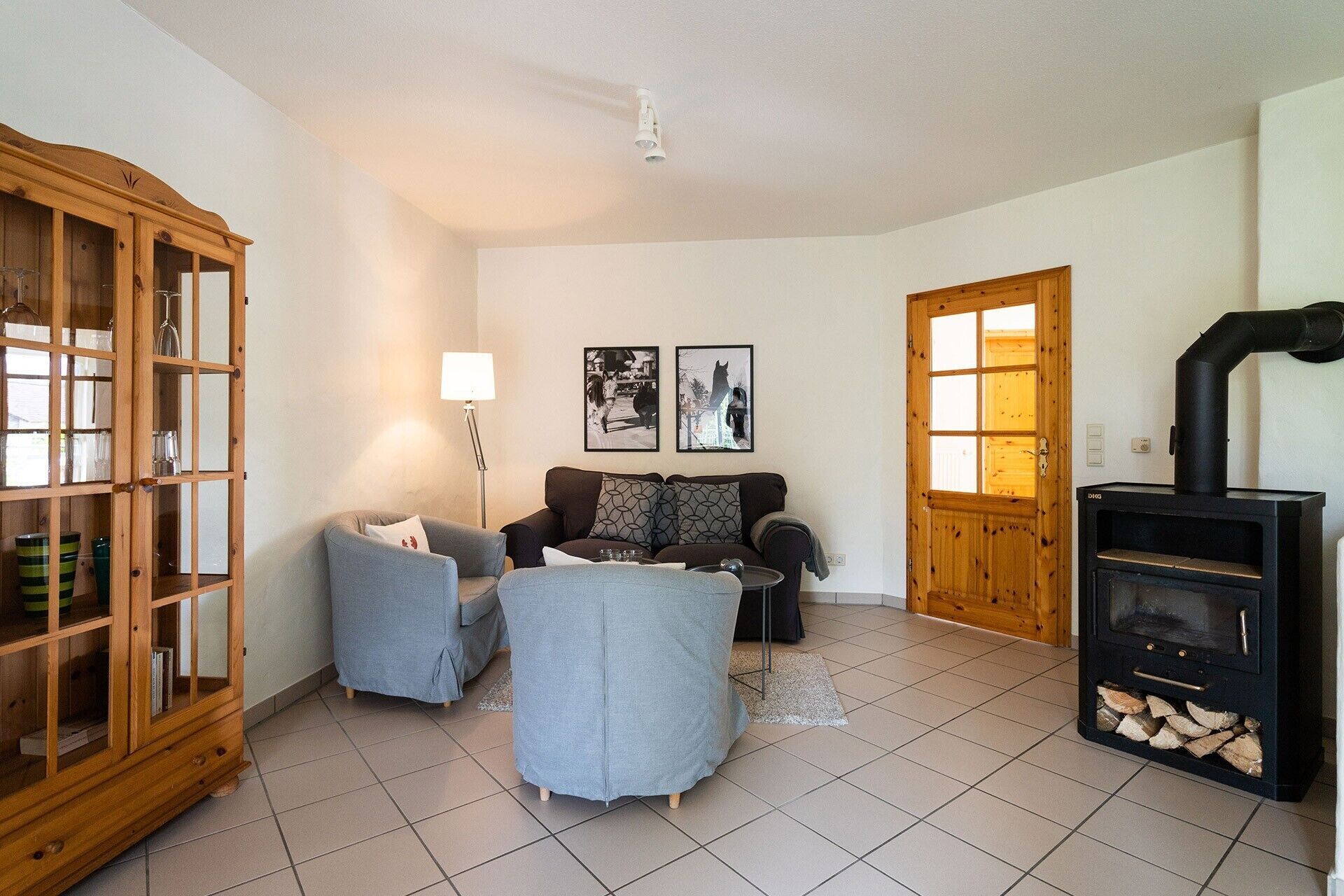 Ein Wohnzimmer mit einer Couch, Sesseln, einem Schrank, einer Lampe, einem Kamin und zwei gerahmten Bildern an der Wand.