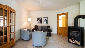 Ein Wohnzimmer mit einer Couch, Sesseln, einem Schrank, einer Lampe, einem Kamin und zwei gerahmten Bildern an der Wand.
