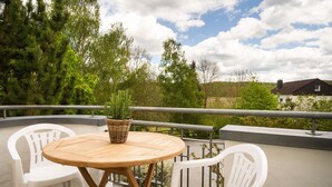A round wooden table with a woven basket on top, surrounded by white plastic chairs on a balcony with a metal railing. - Apartment 'Ferienhof Homann Sauerland - LH 6 Balcony and Wi-Fi' (Brilon)