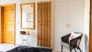Una habitación con puerta de madera, un cuadro enmarcado en la pared, una silla de mimbre con cojín y un felpudo negro en el suelo.