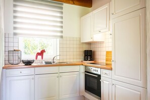 A kitchen with white cabinets, a stainless steel sink, a red chair, and a coffee maker. - Holiday Home 'Ferienhof Homann Sauerland - LH 8' with Shared Terrace and Wi-Fi (Brilon)