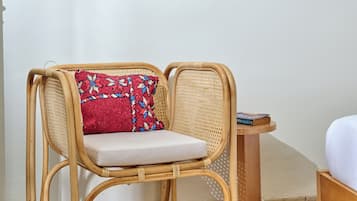 Une chaise en osier avec un coussin, un miroir rond en fibres tressées accroché au mur et une petite table en bois sur laquelle repose un livre.