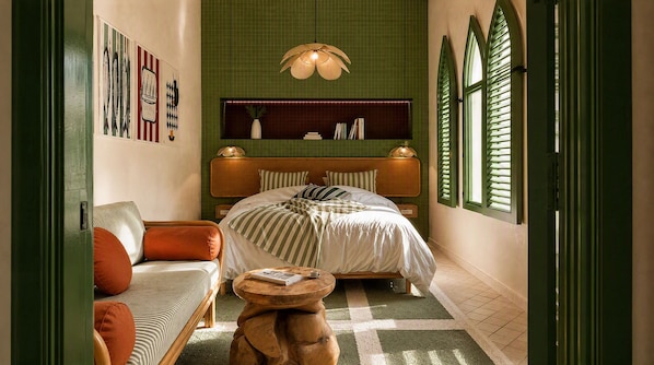 Quarto com cama, sofá, mesa redonda pequena e janela com persianas.