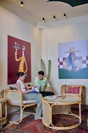 A room with two wicker chairs, a small round table, and a large painting on the wall.