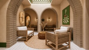 A lounge area with wicker furniture, a central round table, and a green abstract painting on the wall. - StayHere Essaouira Heritage – Dar El Qadima (Essaouira)