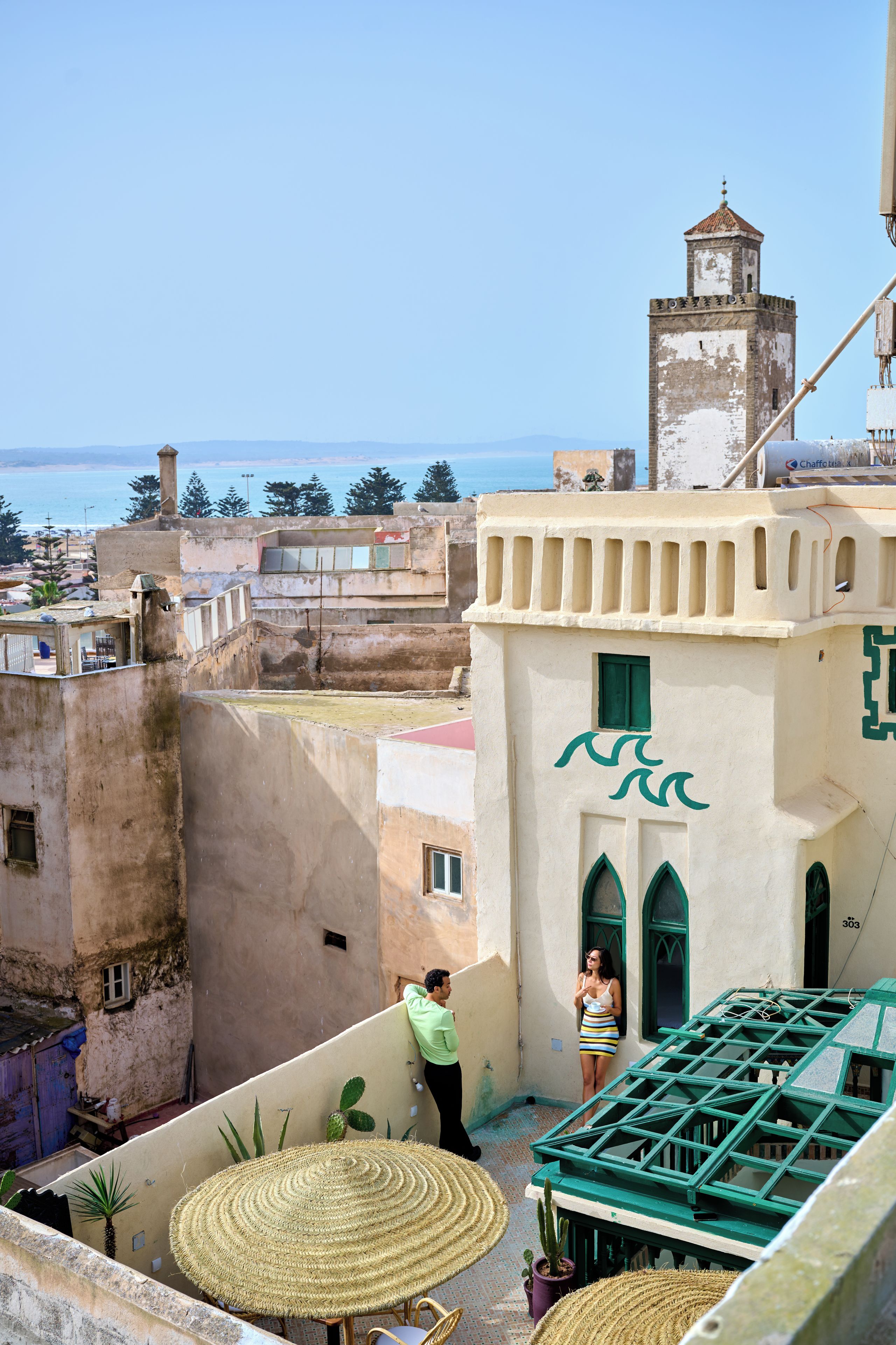Un immeuble doté d’une tour, offrant une vue sur la mer et possédant un balcon avec une table et des chaises.