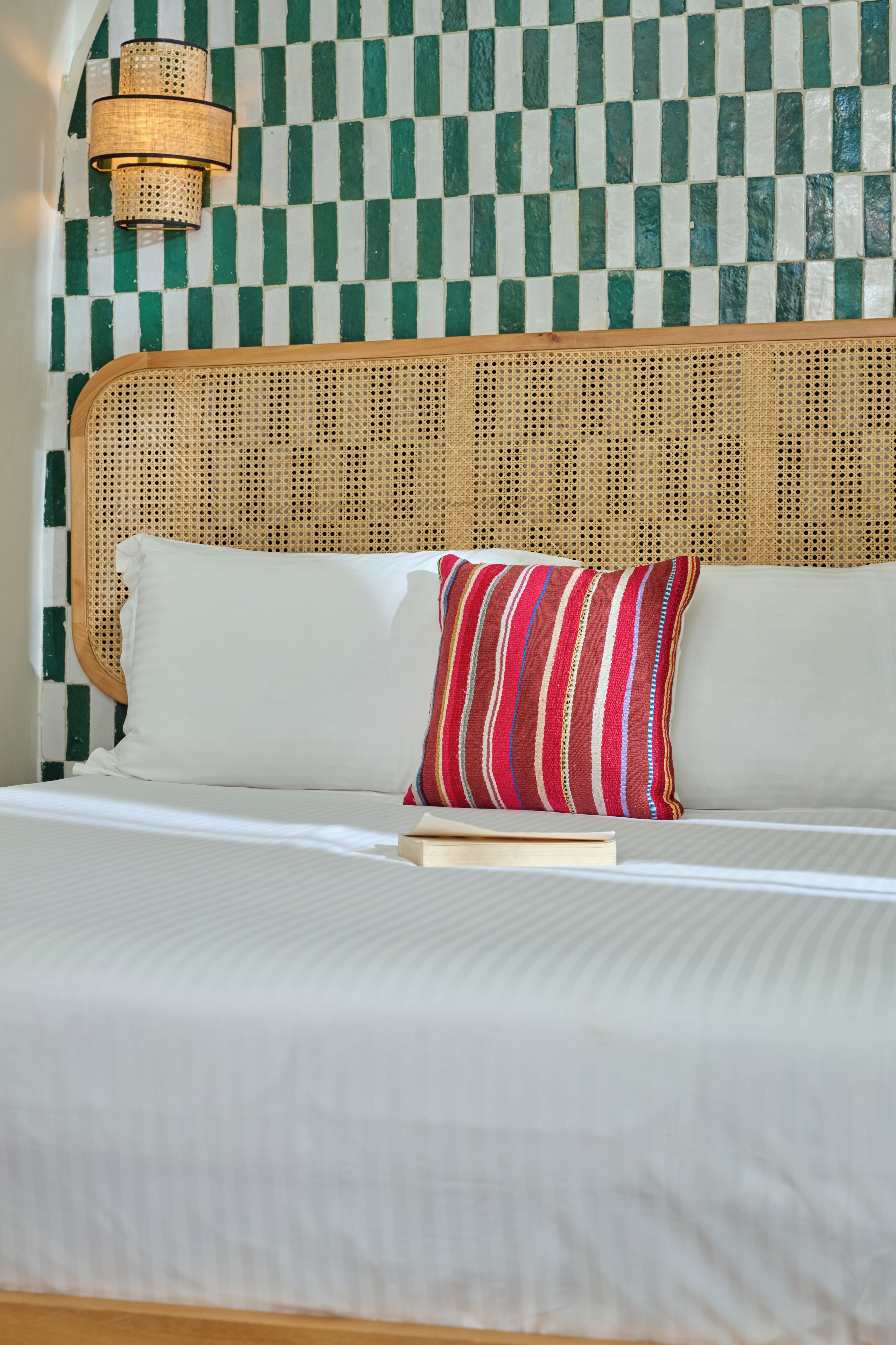 Een bed met witte beddengoed, een gestreept kussen en een geweven hoofdbord.