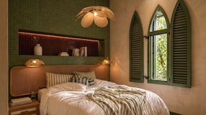 A bedroom with a wicker headboard, a bedside table with a glass, books, and a decorative light fixture. - StayHere Essaouira – Riad Heritage (Essaouira)