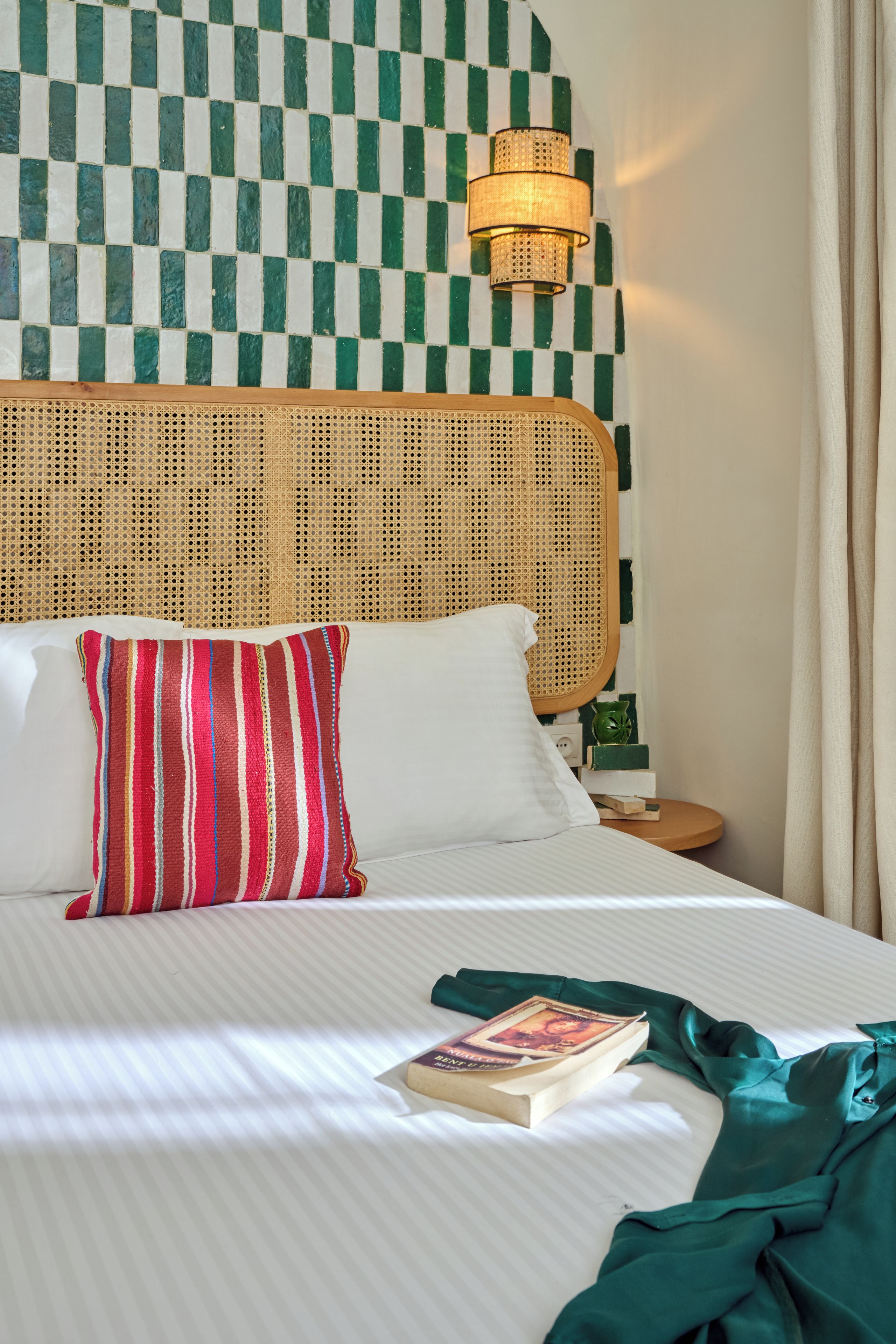 Una cama con un almohadón a rayas, un libro y un paño verde.