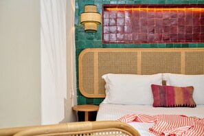 A bed with white and striped bedding, a woven headboard, a small wooden side table, and a wicker chair.
