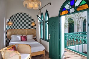 A room with a bed, a chair, a checkered wall, a green door, and a view of the outside. - StayHere Essaouira – Riad Heritage (Essaouira)