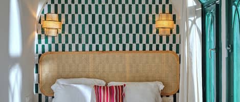 A bed with white linens and a single striped pillow, a checkered wall, and two wall-mounted lamps.